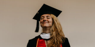 A woman wearing graduation robes smiles with her eyes shut.