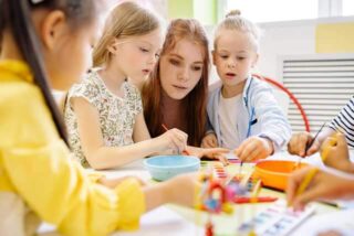 Two children using paintbrushes with their teacher during an art class.